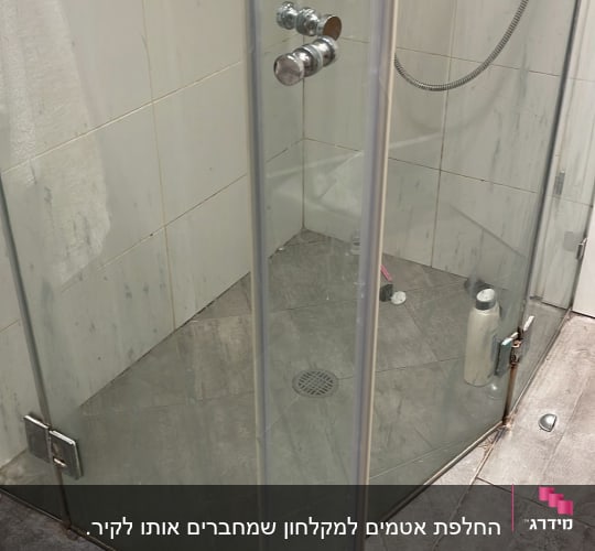 מקלחון זכוכית עם בקבוקי שמפו ומגבת לבנה
